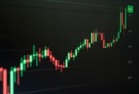 Grafik harga aset kripto yang fluktuatif namun menunjukkan tren pertumbuhan jangka panjang, mencerminkan dinamika pasar digital yang penuh potensi bagi investor cerdas. Tangan seorang investor tampak sedang memegang smartphone dengan aplikasi investasi kripto, menggambarkan keterlibatan personal dalam ekosistem aset digital.