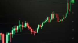 Grafik harga aset kripto yang fluktuatif namun menunjukkan tren pertumbuhan jangka panjang, mencerminkan dinamika pasar digital yang penuh potensi bagi investor cerdas. Tangan seorang investor tampak sedang memegang smartphone dengan aplikasi investasi kripto, menggambarkan keterlibatan personal dalam ekosistem aset digital.