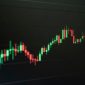 Grafik harga aset kripto yang fluktuatif namun menunjukkan tren pertumbuhan jangka panjang, mencerminkan dinamika pasar digital yang penuh potensi bagi investor cerdas. Tangan seorang investor tampak sedang memegang smartphone dengan aplikasi investasi kripto, menggambarkan keterlibatan personal dalam ekosistem aset digital.