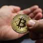 Ilustrasi tangan memegang smartphone menampilkan grafik Bitcoin, melambangkan kemudahan akses dan potensi investasi aset digital. Latar belakang menunjukkan koin Bitcoin yang berkilauan, menggambarkan nilai dan daya tariknya di pasar finansial modern.
