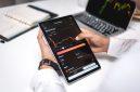 Seorang trader sedang menganalisis grafik pergerakan harga aset kripto pada layar komputer, menunjukkan fokus dan ketelitian yang diperlukan dalam membuat keputusan investasi. Berbagai indikator teknikal terlihat jelas, membantu dalam memprediksi arah pasar.