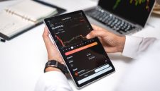 Seorang trader sedang menganalisis grafik pergerakan harga aset kripto pada layar komputer, menunjukkan fokus dan ketelitian yang diperlukan dalam membuat keputusan investasi. Berbagai indikator teknikal terlihat jelas, membantu dalam memprediksi arah pasar.
