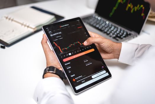 Seorang trader sedang menganalisis grafik pergerakan harga aset kripto pada layar komputer, menunjukkan fokus dan ketelitian yang diperlukan dalam membuat keputusan investasi. Berbagai indikator teknikal terlihat jelas, membantu dalam memprediksi arah pasar.