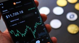 Seorang individu sedang serius memantau pergerakan grafik harga Bitcoin di layar gawai, mencerminkan aktivitas yang sering dilakukan oleh para investor kripto. Gambar ini menunjukkan bagaimana teknologi digital telah mengubah cara kita berinteraksi dengan aset investasi.
