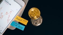 Ilustrasi grafik kenaikan dan penurunan harga Bitcoin yang menunjukkan volatilitas pasar, menjadi pengingat penting bagi investor pemula untuk selalu berinvestasi dengan perencanaan matang dan strategi yang tepat. Sebuah tangan sedang memegang ponsel pintar yang menampilkan aplikasi jual beli aset kripto, menggambarkan kemudahan akses investasi Bitcoin di era digital saat ini.